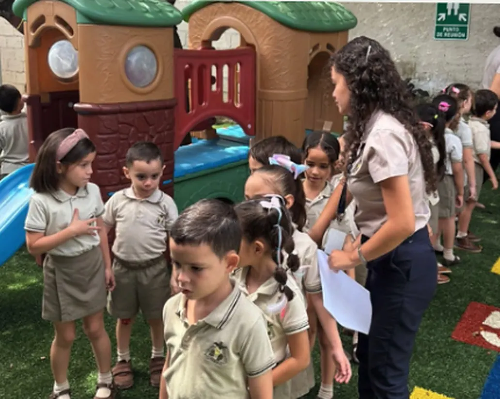 Niños y niñas de preescolar con uniforme beige junto a una docente en el patio de juegos de Centro Educativo La Trinidad