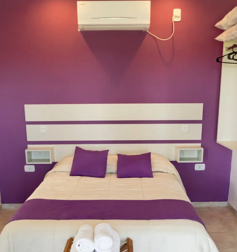 Habitación de monoambiente con cama doble, aire acondicionado y pared violeta